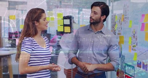 Young professionals discussing strategy with sticky notes and data overlay on glass wall
