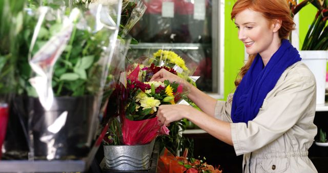Woman smiling and arranging a colorful bouquet of flowers in a flower shop. Bright and cheerful environment indicates fresh flowers and great customer service. Ideal for use in content related to florists, small businesses, plant care, or retail industry.