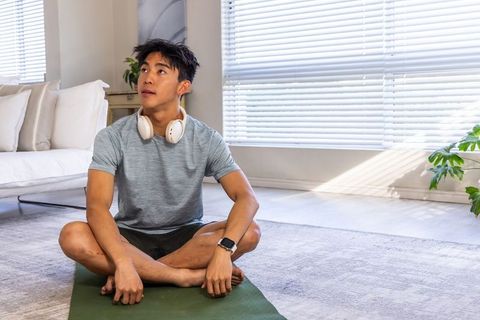 Asian man practicing seated yoga and mindfulness at home with headphones and smartwatch