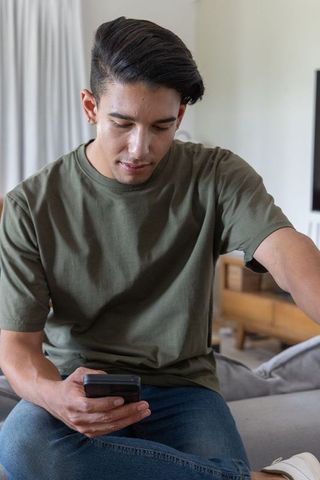 African man sitting on sofa using smartphone at home casual lifestyle daylight interior