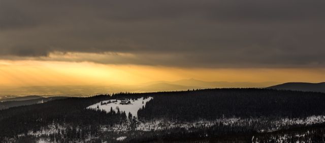 Golden sun rising over snow-covered, forested hills, creating a serene and tranquil winter landscape. Ideal for conveying themes of nature, beauty, tranquility, and dramatic scenery. Perfect for travel, seasonal, and nature-related projects, such as calendars, postcards, and promotional materials for winter destinations.