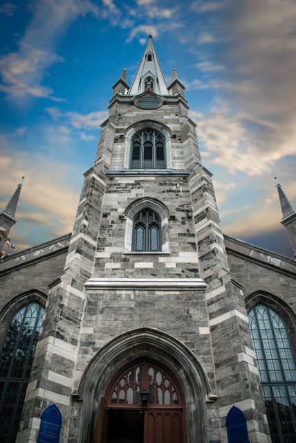Grand view of a historical stone church with Gothic architectural elements, including steeples and arches, set against a dramatic evening sky. Perfect for religious event promotions, historical architecture features, and travel guides highlighting historical landmarks.