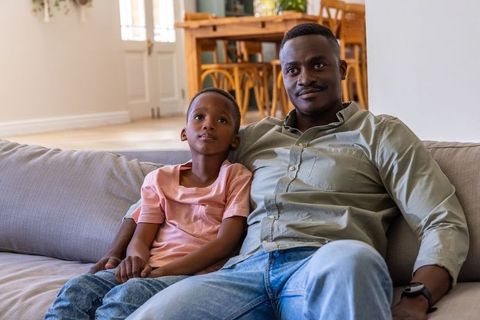 African american father and son relaxing on sofa in cozy living room, bonding moment