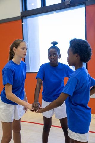 Diverse teen female athletes displaying team unity in gym