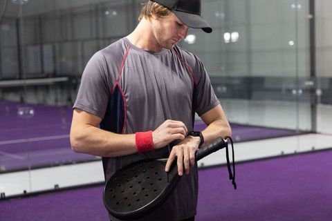 Padel player checking smartwatch on purple indoor court