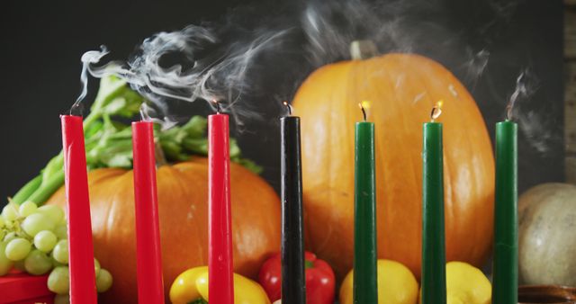 This vibrant display showcases the Kwanzaa Kinara with smoking wick candles in red, black, and green, symbolizing the African heritage and the values celebrated during the holiday. The background includes pumpkins, grapes, bell peppers, and various green vegetables, emphasizing the seasonal harvest and abundance. Ideal for illustrating cultural celebrations, educational content about Kwanzaa, and community event promotions.