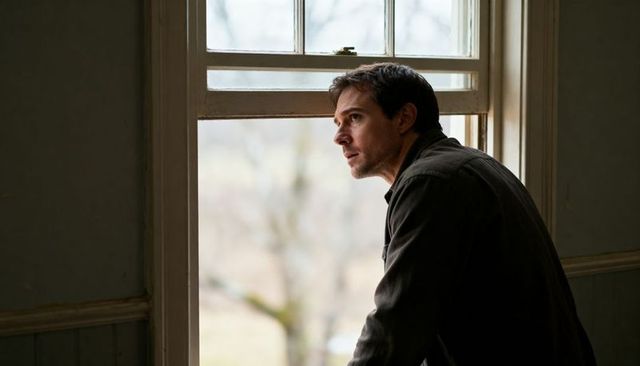 Contemplative man leaning at window gazing outside through sash window soft natural light