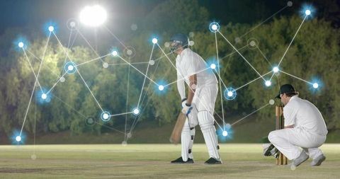 Batsman holding bat with wicketkeeper crouching under floodlights, digital analytics overlay