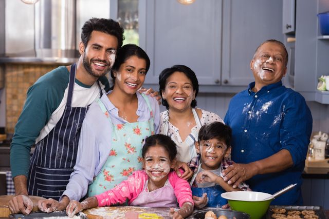 Multi-generation family having fun while baking together in a home kitchen. Parents, children, and grandparents all smile with faces dusted in flour, showcasing their happiness and bond. Ideal for use in advertisements, family-oriented content, family bonding, or cooking-related themes, highlighting togetherness and joy in familial activities.