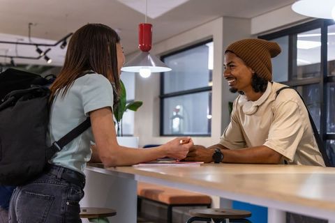 Young diverse coworkers chatting at modern coworking counter with backpacks and headphones