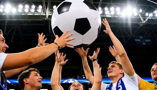 Fans reaching for giant soccer ball under stadium lights cheering during victory moment