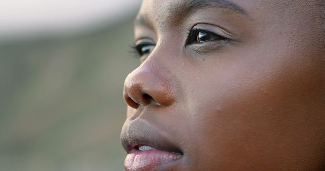 This close-up image depicts an African American woman looking thoughtfully into the distance. Ideal for use in projects emphasizing introspection, calmness, natural beauty, and meditation themes. Excellent for use in advertisements, promotional materials, and content focusing on personal growth, wellness, and mindfulness.