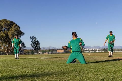 Triumphant outfielder kneeling and celebrating with green-uniform teammates on baseball field