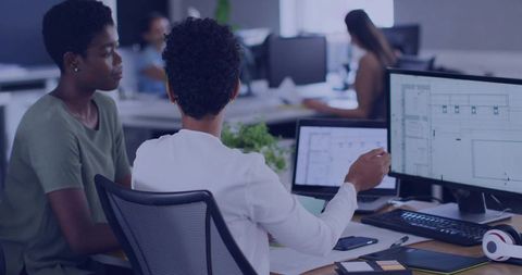 Colleagues Collaborating on Architectural Plans at Dual-Monitor Desk in Modern Office