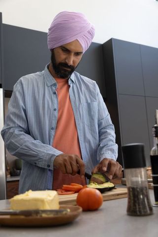 Indian man wearing turban preparing avocado and tomato in modern kitchen