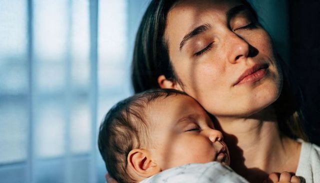 Mother cradling sleeping newborn by window light, tender bonding and quiet rest