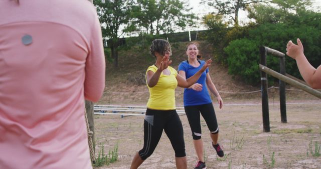 Women enjoying a fitness session in an outdoor park, exchanging high fives and motivating each other. Ideal for use in articles, advertisements, or websites promoting community fitness programs, women's health and wellness, team-building activities, and active lifestyles.