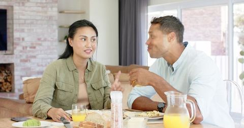 Couple sharing relaxed breakfast and chatting at sunlit dining table with orange juice