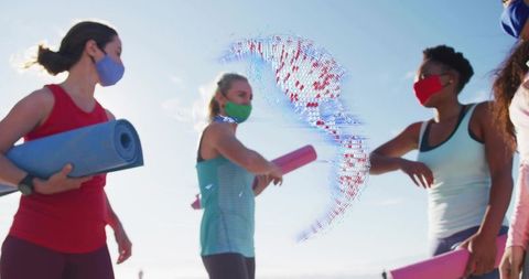 Women greeting on beach wearing masks holding yoga mats as smartwatch hologram floats