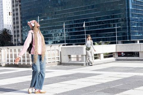 Carefree diverse young women enjoying city rooftop, listening to music, streetwear fashion