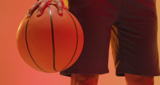Image of mid section of biracial male basketball player with ball on orange to yellow background. Sports and competition concept.