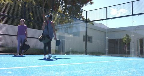 Sunlit padel players walking on bright blue court carrying paddles and sports bags