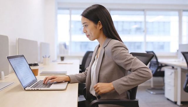 Typing Asian businesswoman working on laptop in modern open-plan office