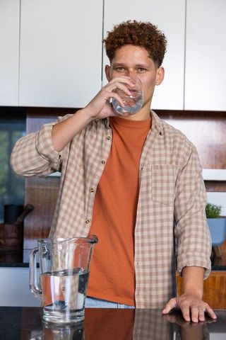 Young man drinking water in modern kitchen promotes healthy lifestyle