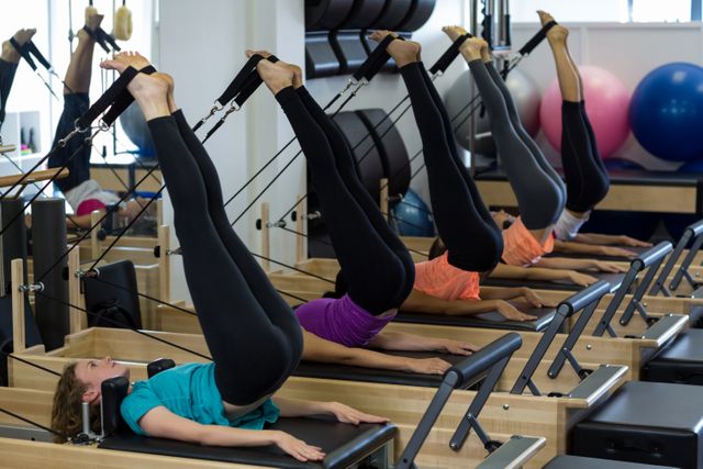 Women are engaging in rigorous Reformer Pilates exercises, focusing on building core strength and enhancing flexibility. Ideal for use in fitness and wellness content, showcasing group training sessions, or illustrating Pilates techniques.