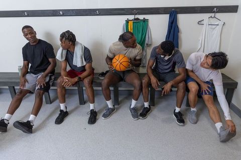Multiracial basketball team relaxing on locker bench holding ball and stretching together