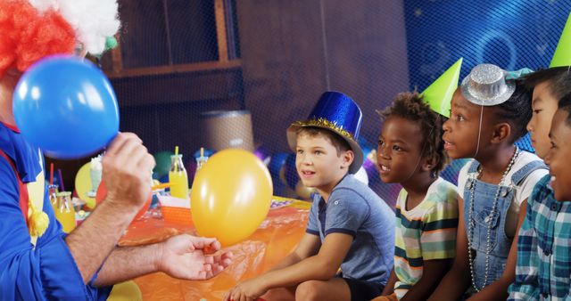 A clown entertains a group of diverse children at a birthday party, inflating balloons with copy space. Their expressions of anticipation and joy suggest a lively and fun atmosphere.