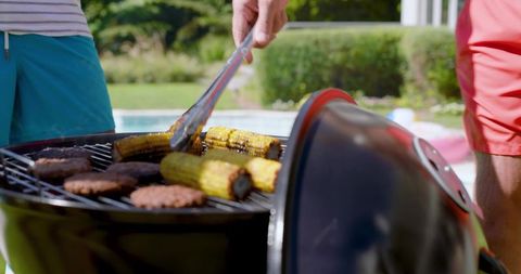 Friends Grilling Corn and Burgers by Pool on Sunny Day