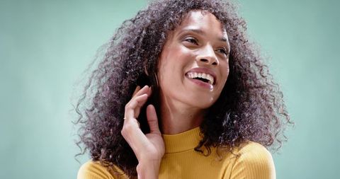 Joyful African American woman smiling in mustard turtleneck with hoop earrings touching ear