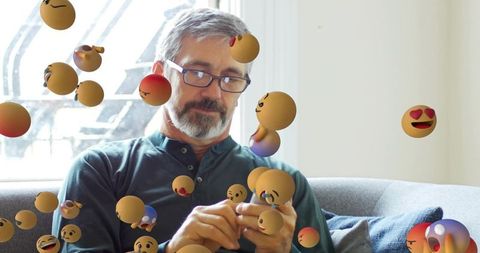 Mature man using smartphone with augmented reality floating emoji spheres in sunlit lounge