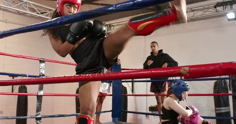 Female fighter rising after knockdown delivering high training kick in boxing ring