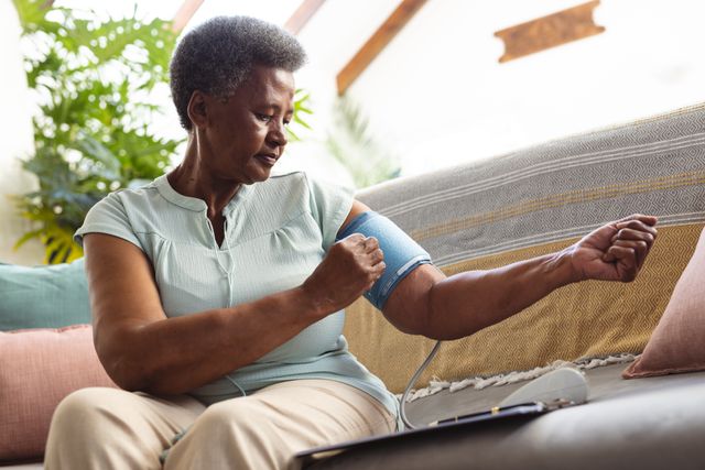 Low angle view of african american senior woman examining blood pressure with gauge on sofa at home. Short hair, unaltered, hypertensive, healthcare, sickness, retirement and home concept.