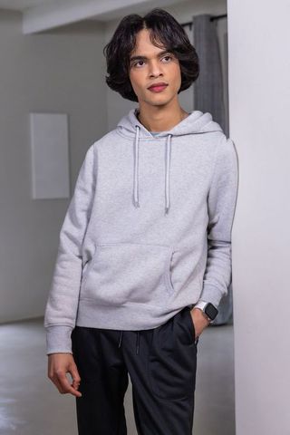 Teen male leaning against partition wearing gray hoodie and smartwatch in minimalist interior