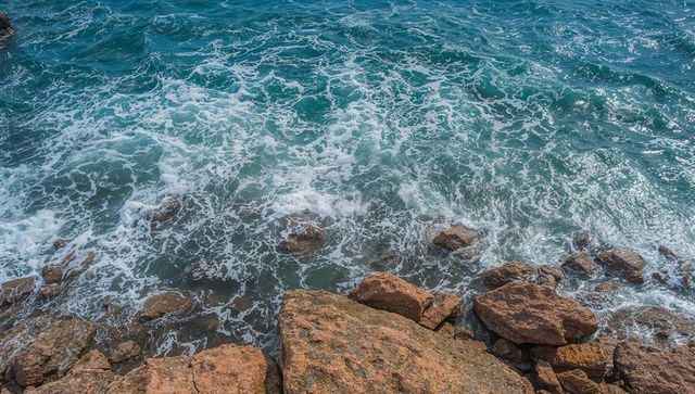 Overhead turquoise waves crashing on rugged rocky coastline with weathered boulders