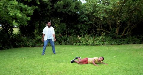 African american father and son playing and laughing on backyard lawn in sunny garden