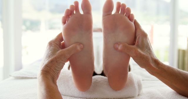 A pair of Caucasian senior feet are being held, suggesting a foot examination or massage, with copy space. It indicates a healthcare or wellness setting, involving a podiatrist or a massage therapist.