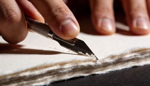 Hand guiding scalpel cutting handmade paper fibers closeup macro for bookbinding crafts