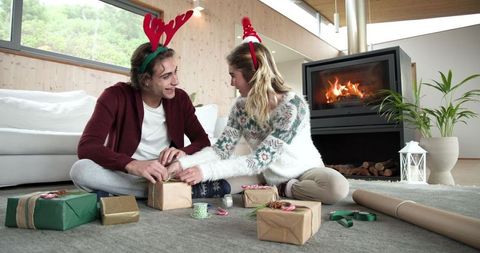 Festive friends wrapping holiaday gifts by cozy fireplace