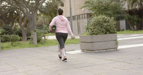 Mature woman walking through urban plaza carrying yoga mat and water bottle