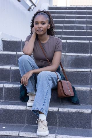 Young african woman sitting on urban steps wearing casual denim and crossbody leather bag