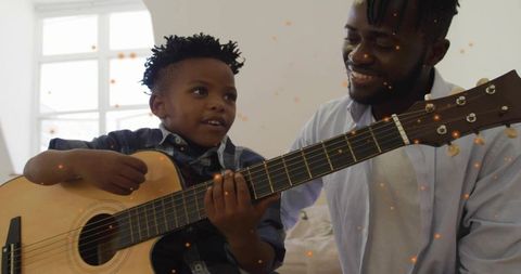 Father teaching son acoustic guitar, smiling bonding during home music lesson