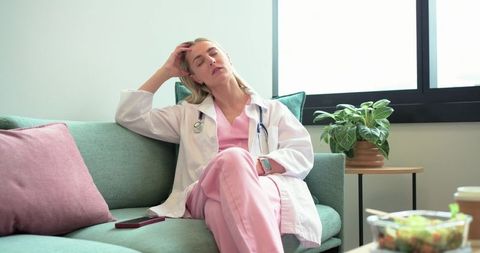 Fatigued nurse resting on breakroom sofa after long shift, healthcare worker burnout