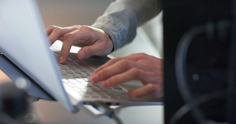 Mid-adult man typing on silver laptop at minimalist home office desk with usb-c stand