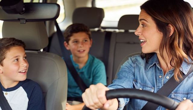 Smiling mother driving with two boys engaging in lively family conversation during car ride