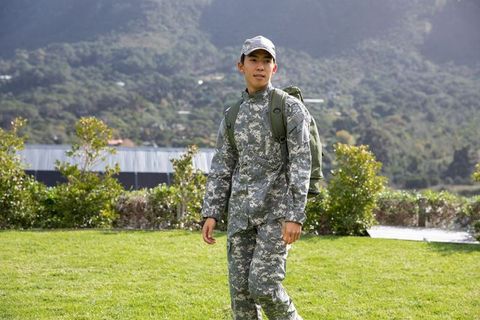 Asian soldier walking on grassy training ground wearing camouflage uniform with olive backpack