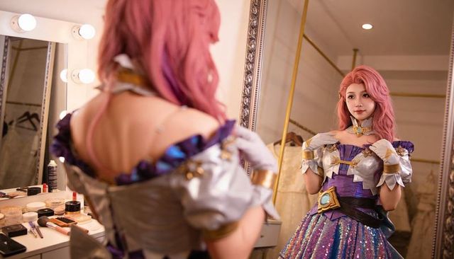 Asian cosplayer adjusting choker at vanity in purple sequined fantasy costume backstage